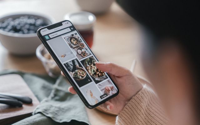 Main tenant un téléphone affichant une liste de recettes, posé sur une table de cuisine