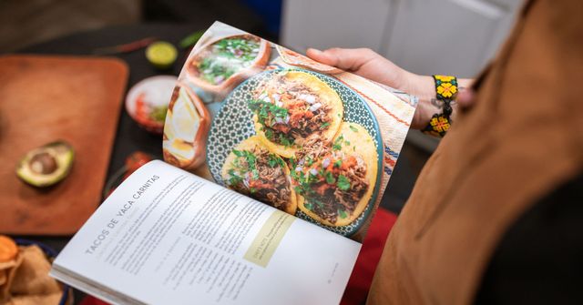 Mains feuilletant un livre de cuisine ouvert sur une recette, entouré d'ingrédients frais